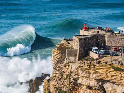 Acantilado con faro, olas gigantes y personas observando desde la cima. Surfers en el mar.