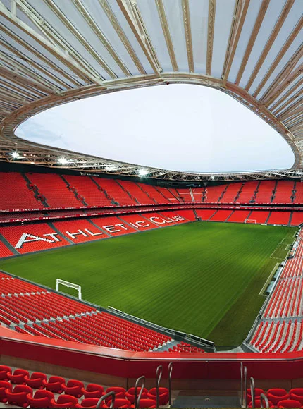 Estadio vacío con gradas rojas y césped verde, vista desde arriba.
