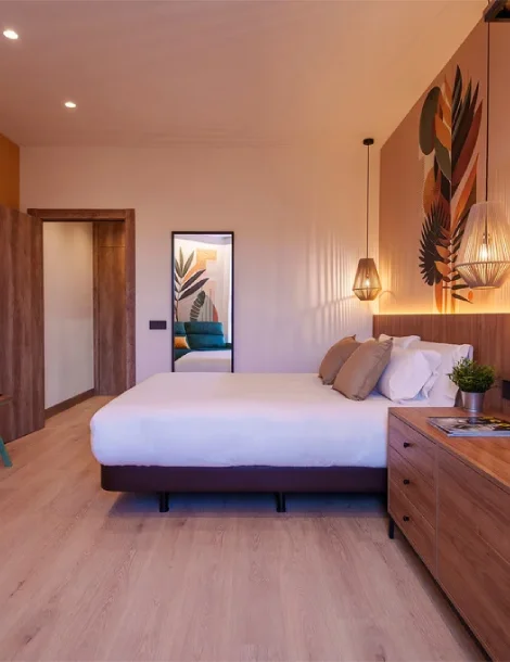 Habitación moderna con cama, lámparas colgantes y decoración vegetal en la pared.