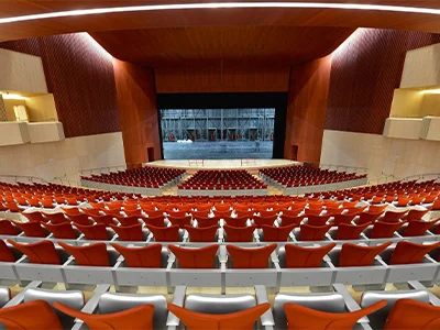 Auditorio con asientos rojos y un gran escenario vacío al frente.