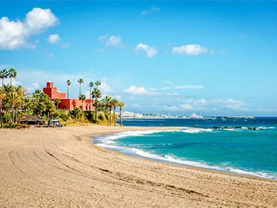 Playa tropical con palmeras, edificio rojo y cielo azul con nubes esponjosas.