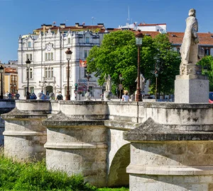 Puente de piedra con estatuas y un edificio histórico al fondo en un día soleado.