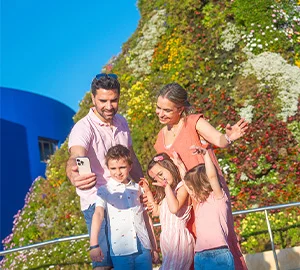 Familia sacándose una selfie frente a un colorido jardín vertical en un día soleado.