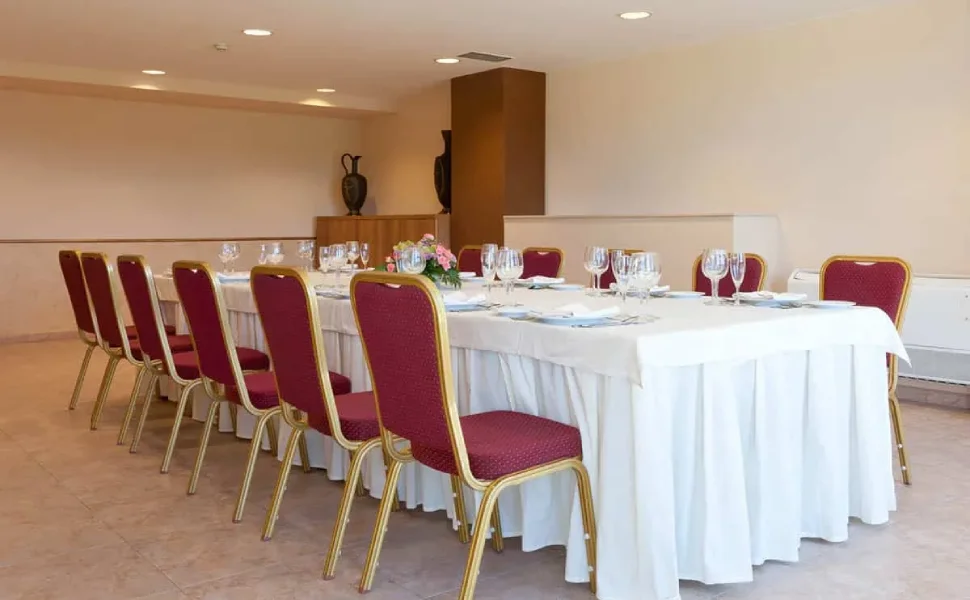Mesa rectangular con sillas rojas y copas listas en salón vacío.