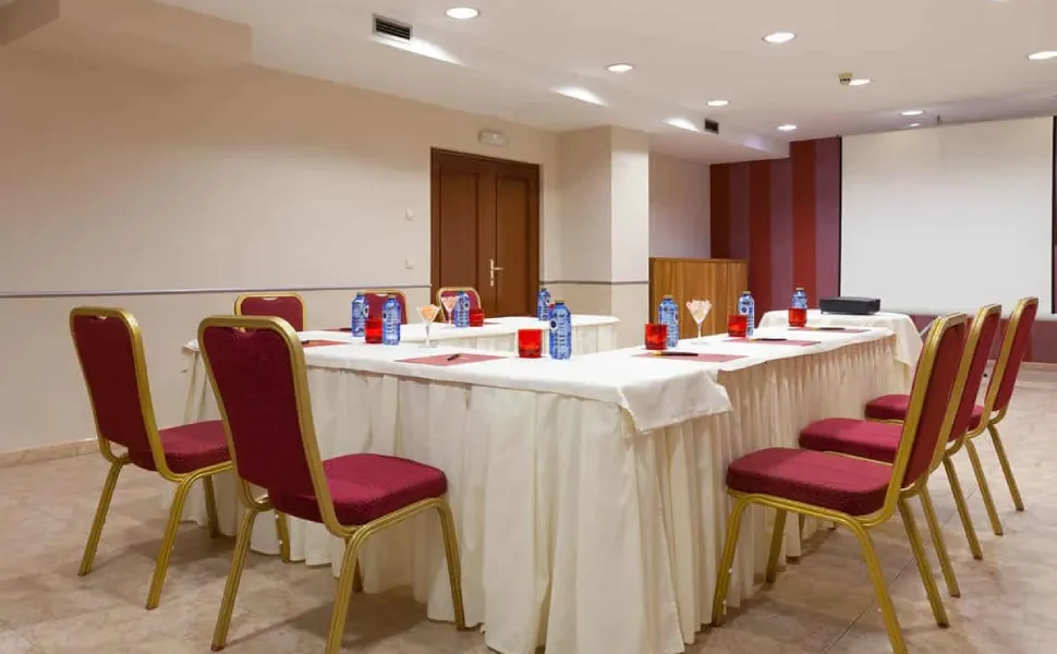 Sala de reuniones vacía con mesa en U y sillas rojas.