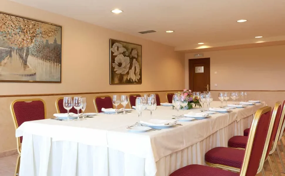 Sala de reuniones con mesa larga y copas de cristal, decorada con cuadros.