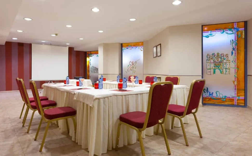 Sala de conferencias con mesa, sillas rojas y botellas de agua sobre manteles blancos.