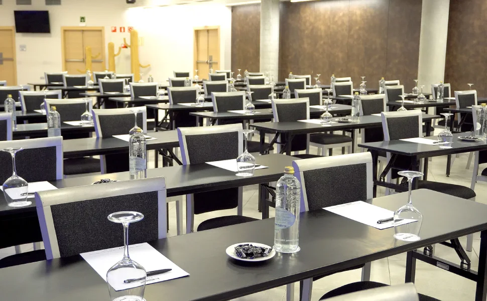 Sala de conferencias con mesas preparadas, copas y botellas de agua.