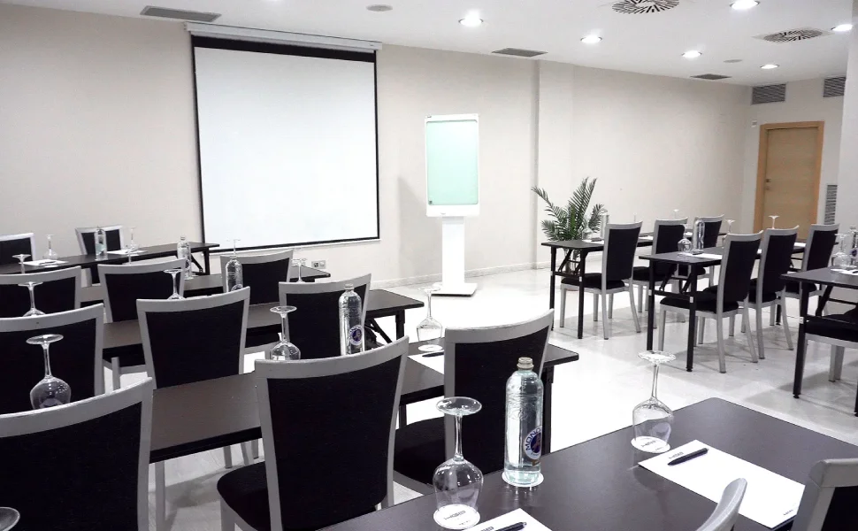 Sala de conferencias con mesas, sillas y proyector.