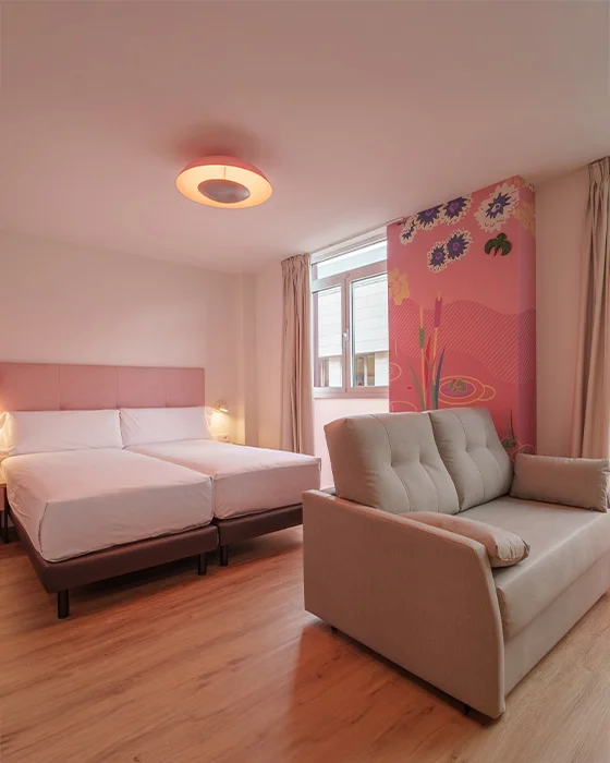 Habitación moderna con cama doble, sofá beige y pared decorativa floral rosa.