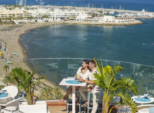 Pareja disfrutando de una vista al mar en una terraza junto a la playa.