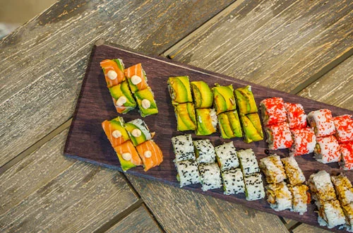 Tabla con variedad de sushi sobre mesa de madera.