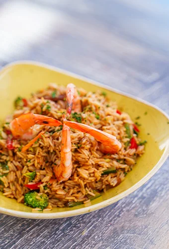 Arroz frito con camarones, verduras y especias en un tazón amarillo.