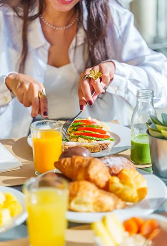 Persona preparando un desayuno con jugo, tostadas y croissants.