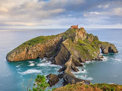 Una isla rocosa con un camino de piedra que lleva a una ermita en la cima, rodeada de mar.
