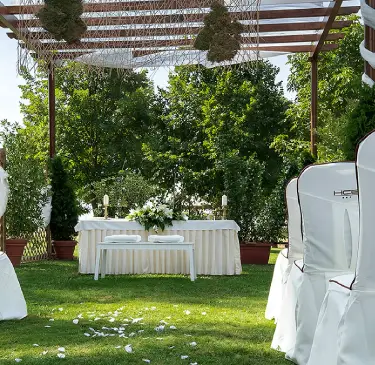 Ceremonia al aire libre con altar decorado y sillas blancas en un jardín verde.