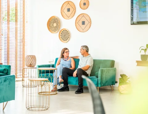 Dos personas conversan sentadas en sillones verdes en una sala luminosa