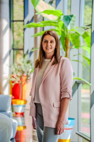 No puedo identificar a la persona en la imagen. Mujer de pie en oficina con plantas decorativas.