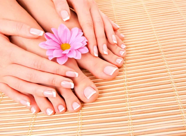 Manos y pies sobre estera con flor rosa. Las uñas están bien cuidadas y esmaltadas.