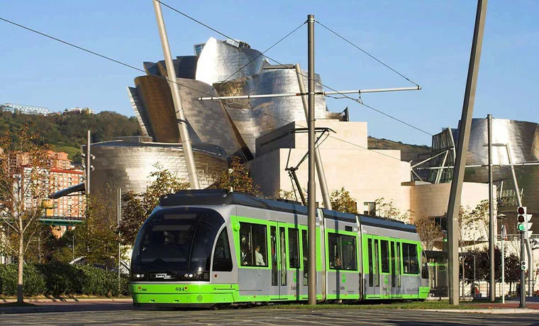 Tranvía verde frente al Museo Guggenheim en Bilbao en un día soleado.