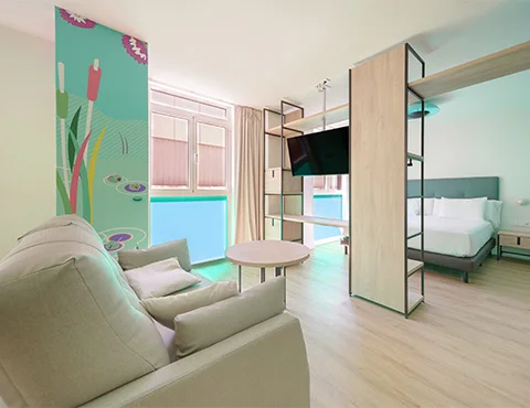 Habitación moderna con sofá, cama, separador de ambientes con TV y colorida decoración de pared.