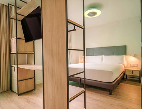 Habitación moderna con cama doble, mueble divisor con TV y luz de techo circular.