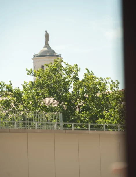 Torre con estatua detrás de árboles bajo un cielo despejado.