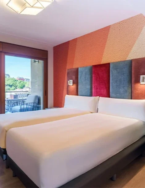Habitación de hotel con dos camas y un balcón con vista al exterior.