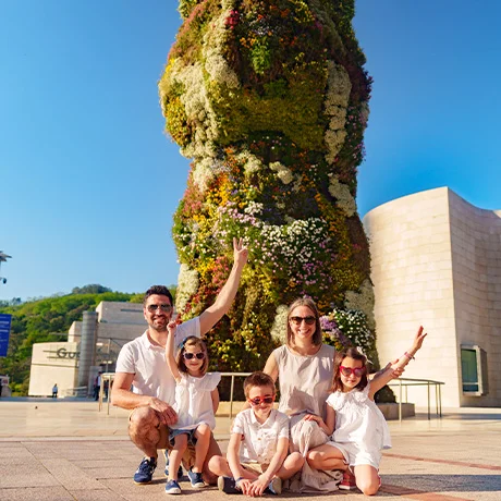 Familia sonriente frente a una gran figura vegetal en un día soleado.
