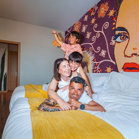 Una familia feliz apilada sobre una cama grande en una habitación con un mural colorido en la pared.