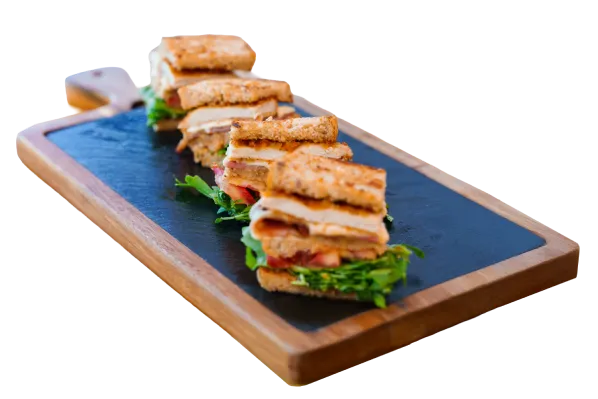 Sándwiches apilados en una tabla de cortar de madera con lechuga y tomate.