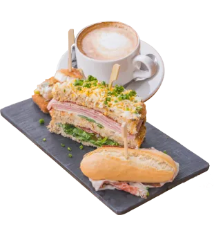 Sándwich variado con café con leche en una bandeja de pizarra.