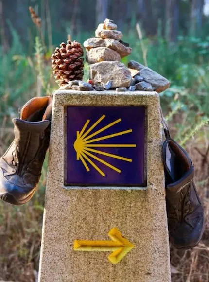 Hito del Camino de Santiago con conchas, botas y flecha amarilla.