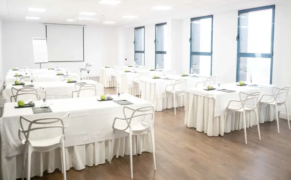 Aula luminosa con mesas blancas y sillas, lista para un evento o presentación.