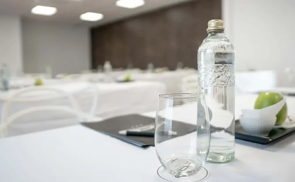 Botella de agua, vaso y manzana verde sobre mesa de conferencia blanca.