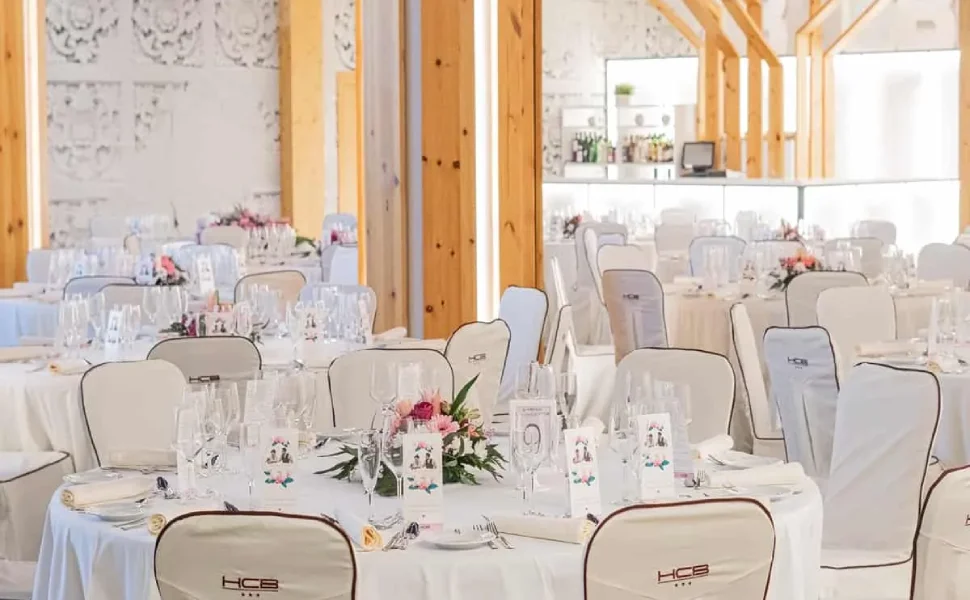 Salón de banquete elegante con mesas decoradas y sillas cubiertas.