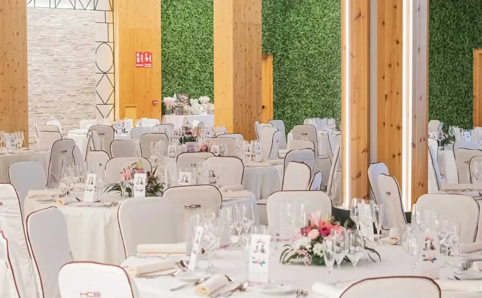 Salón de eventos decorado con mesas blancas y paredes con plantas verdes.