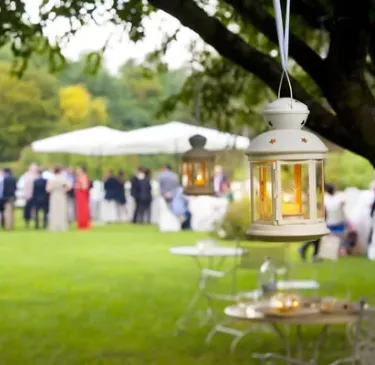 Linterna colgante en un jardín, con gente al fondo en un evento al aire libre.