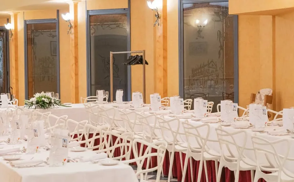 Sala para banquete con mesas largas, sillas blancas y decoración elegante.