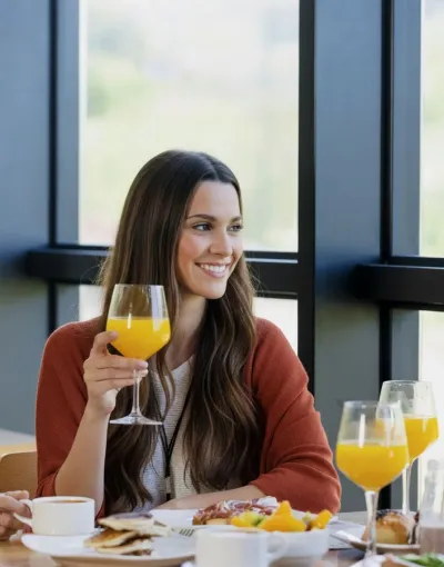 Mujer sonriendo mientras sostiene una copa de jugo de naranja en un restaurante luminoso.