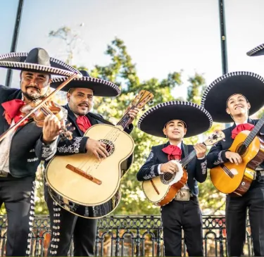 Grupo de mariachis tocando instrumentos en un parque al aire libre.