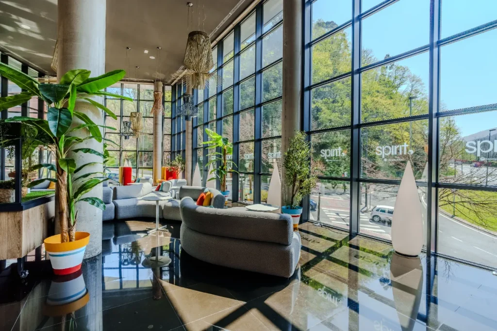 Salón moderno con sofás curvos, plantas y ventanas amplias con vista al exterior.