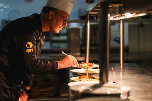 Chef decorando platos en una cocina profesional iluminada. Lleva gorro y uniforme de chef. Chef decorando platos en una cocina profesional iluminada. Lleva gorro y uniforme de chef.