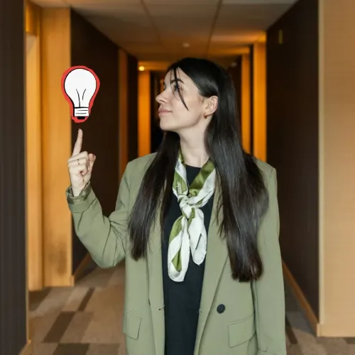 Mujer con saco señalando un dibujo de bombilla roja en un pasillo iluminado.