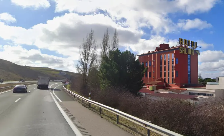 Carretera con coches, hotel rojo a la derecha, cielo azul con nubes.