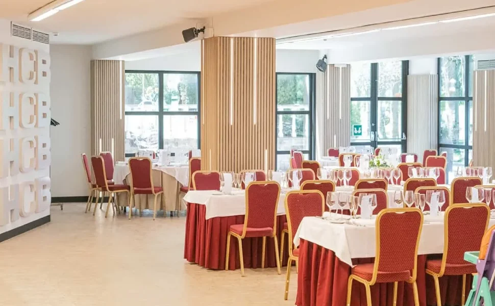 Sala de eventos con mesas redondas y sillas rojas, decorada para una ocasión especial.