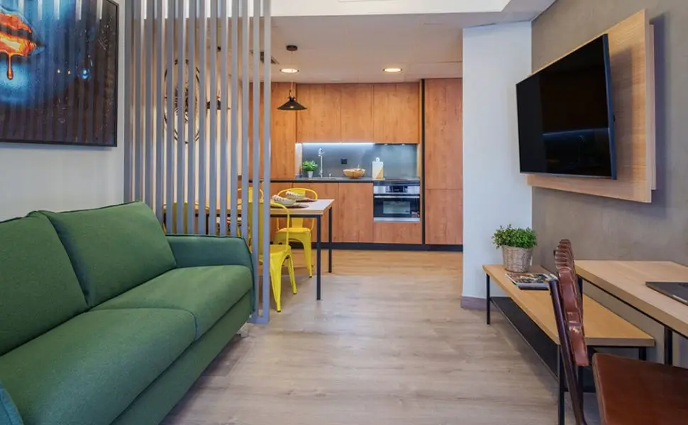 Sala moderna con sofá verde y cocina de madera en el fondo.