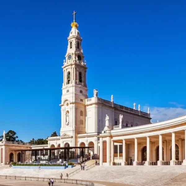 Iglesia con torre y cruz bajo un cielo azul claro, rodeada de columnatas.