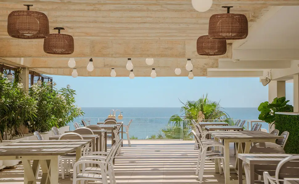 Terraza de restaurante con vista al mar y muebles de madera blanca.