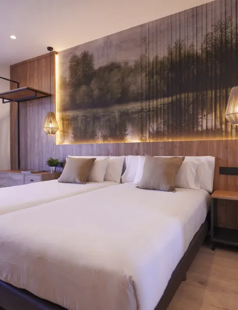 Cama doble en habitación moderna con decoración de paisaje y luz cálida en el cabecero.